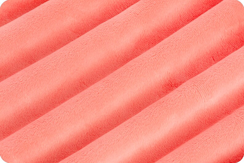 Puede incluir: Primer plano de una tela suave de color coral con textura peluda. La tela est&aacute; doblada en un patr&oacute;n ondulado, creando un aspecto suave y fluido.