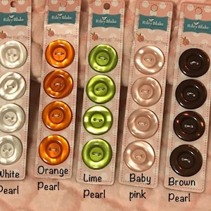 May include: Five cards with six pearl buttons each, displayed in a row. The buttons are in five colors: white, orange, lime green, baby pink, and brown. The cards have the text "Riley Blake" and "Sew Together" printed on them.