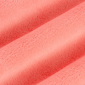 Puede incluir: Primer plano de una tela suave de color coral con una textura peluda. La tela est&aacute; doblada y tiene un ligero brillo.