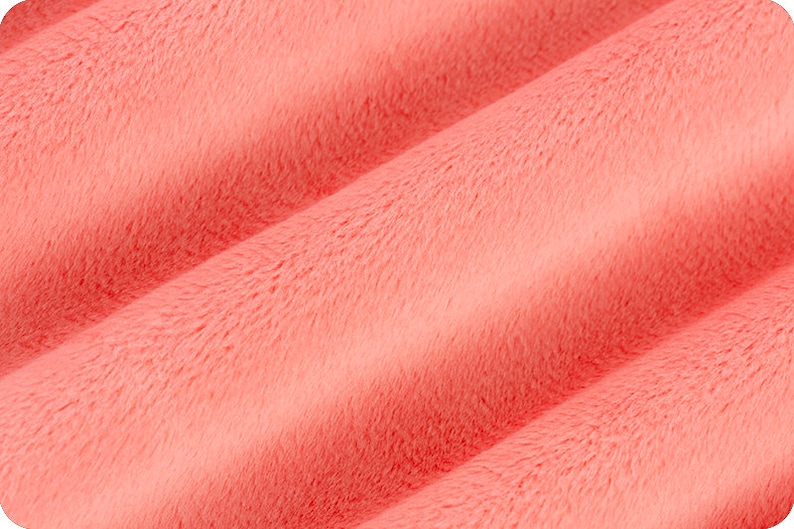 Puede incluir: Primer plano de una tela suave de color coral con una textura peluda. La tela est&aacute; doblada y tiene un ligero brillo.