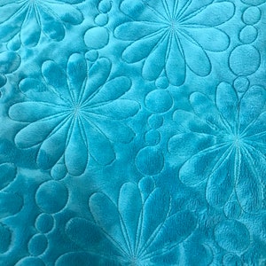 May include: Close-up of a turquoise blue fabric with a quilted pattern of stylised flowers and circles.