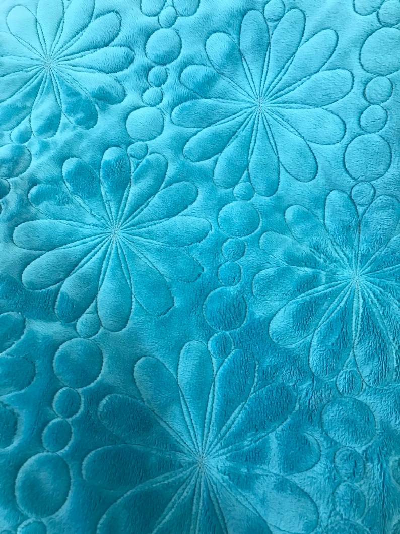 May include: Close-up of a turquoise blue fabric with a quilted pattern of stylised flowers and circles.