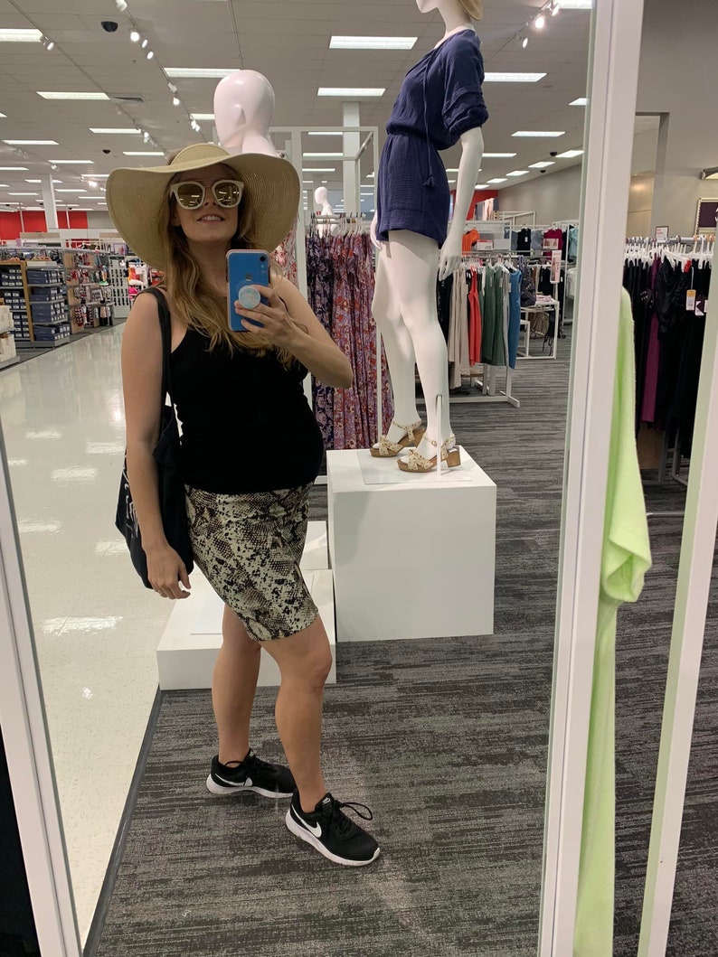 Puede incluir: Una mujer con un top negro de tirantes, una falda estampada en marr&oacute;n y blanco y zapatillas negras. Lleva un sombrero de paja de ala ancha y gafas de sol. Est&aacute; de pie frente a un espejo en una tienda de ropa.