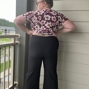 Puede incluir: Una mujer con una blusa de estampado floral marr&oacute;n y pantalones negros de pierna ancha.