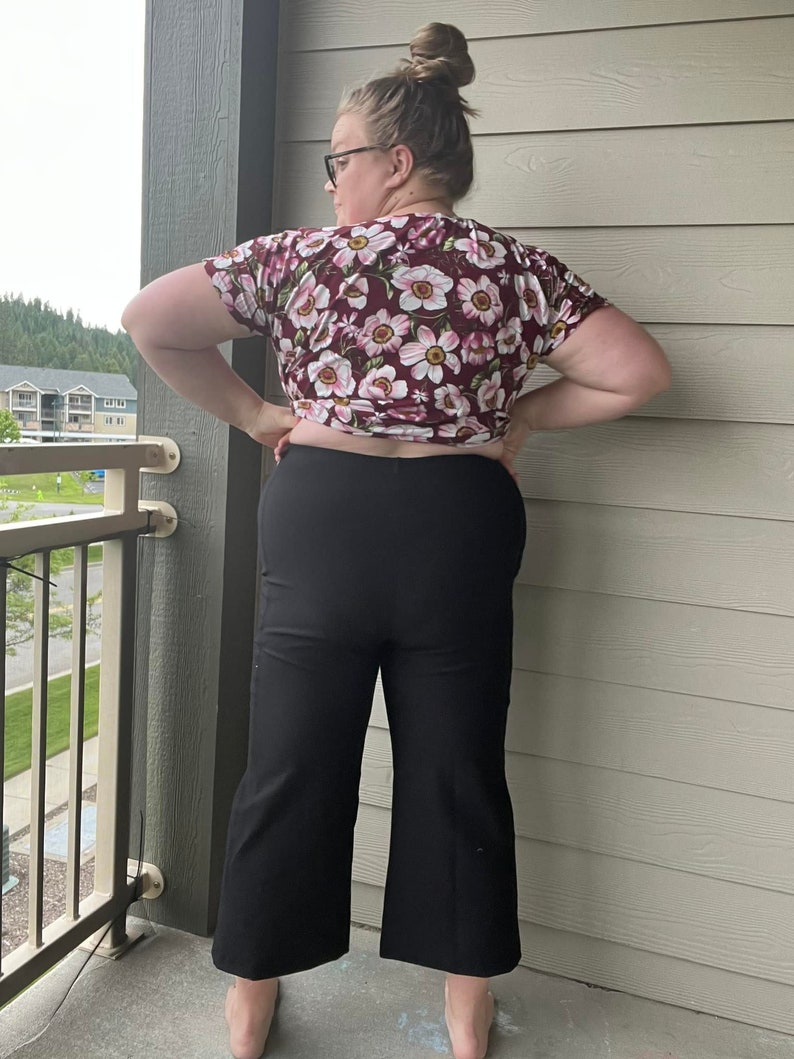 Puede incluir: Una mujer con una blusa de estampado floral marr&oacute;n y pantalones negros de pierna ancha.