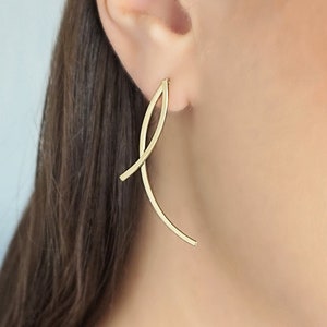 Peut inclure: Une paire de boucles d'oreilles dorées avec un design simple et abstrait. Les boucles d'oreilles sont longues et fines, avec une forme incurvée qui ressemble à une feuille ou à une vague.
