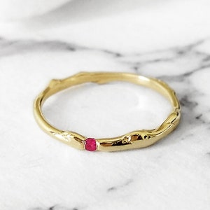 Puede incluir: Un anillo de oro con una banda texturizada en forma de rama y una sola piedra preciosa rosa pequeña.