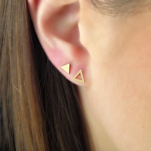 May include: A pair of gold triangle stud earrings. The earrings are small and delicate, and they are perfect for everyday wear.