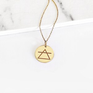 May include: Gold necklace with a round pendant featuring a geometric symbol. The symbol is a triangle with a horizontal line across the middle.