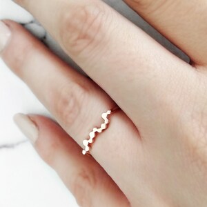 May include: A rose gold ring with a wavy design. The ring is made of small, round beads that are connected together to create a wavy pattern.