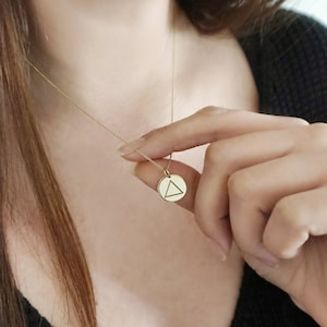 May include: A gold chain necklace with a small round pendant featuring a triangle design.