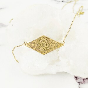 May include: A gold necklace with a diamond-shaped pendant featuring a detailed mandala design.
