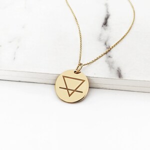 May include: Gold necklace with a round pendant featuring an engraved symbol of an upside-down triangle with a horizontal line through it.