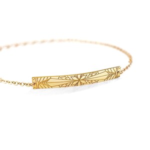 May include: A gold chain bracelet with a rectangular charm featuring a geometric design.