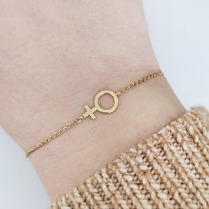 May include: A gold chain bracelet with a delicate female symbol charm.