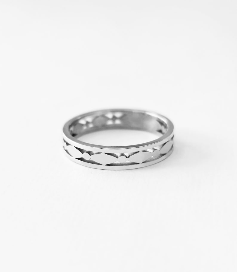 May include: A silver ring with a repeating pattern of cut-out shapes. The ring is circular and has a polished finish. The design features a series of elongated, diamond-like cutouts around the band, creating an openwork effect. The ring is set against a white background.