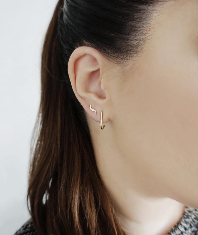 May include: A person wearing a pair of gold hoop earrings and a small gold curved earring in their left ear.