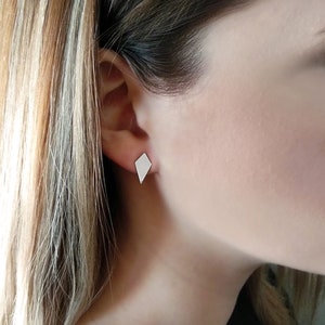 May include: A pair of silver diamond-shaped stud earrings. The earrings are small and simple, and they would be a great addition to any jewelry collection.