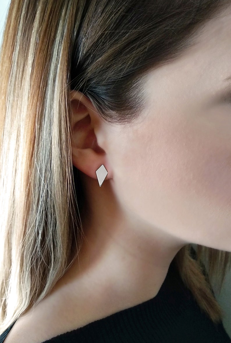 May include: A pair of silver diamond-shaped stud earrings. The earrings are small and simple, and they would be a great addition to any jewelry collection.