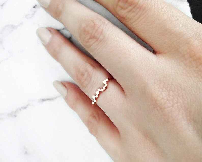 May include: A rose gold ring with a wavy design. The ring is made of small, round beads that are connected together to create a wavy pattern.