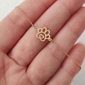 May include: A gold chain necklace with a delicate paw print charm featuring a heart in the center.