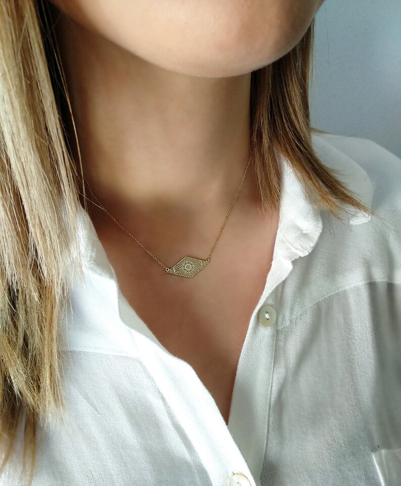 May include: A gold necklace with a diamond-shaped pendant featuring a detailed eye design.