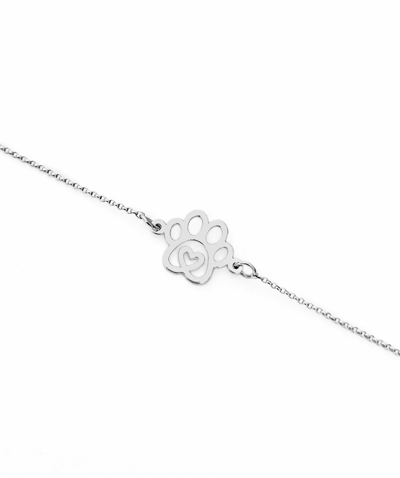 May include: A silver chain bracelet with a paw print charm featuring a heart inside. The charm is a delicate cutout design.