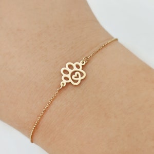 May include: A gold chain bracelet with a paw print charm featuring a heart in the center.