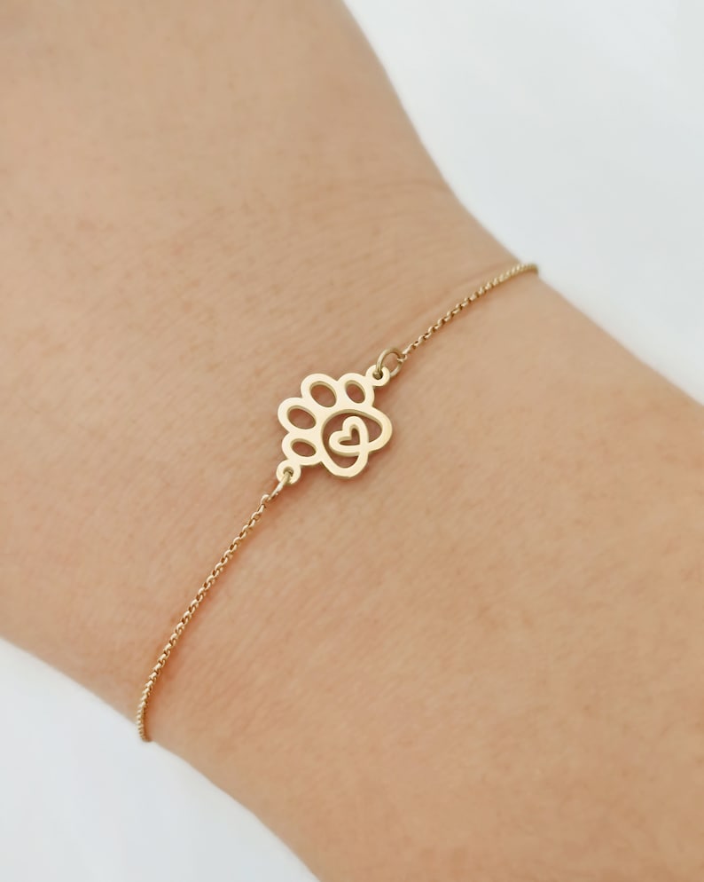 May include: A gold chain bracelet with a paw print charm featuring a heart in the center.