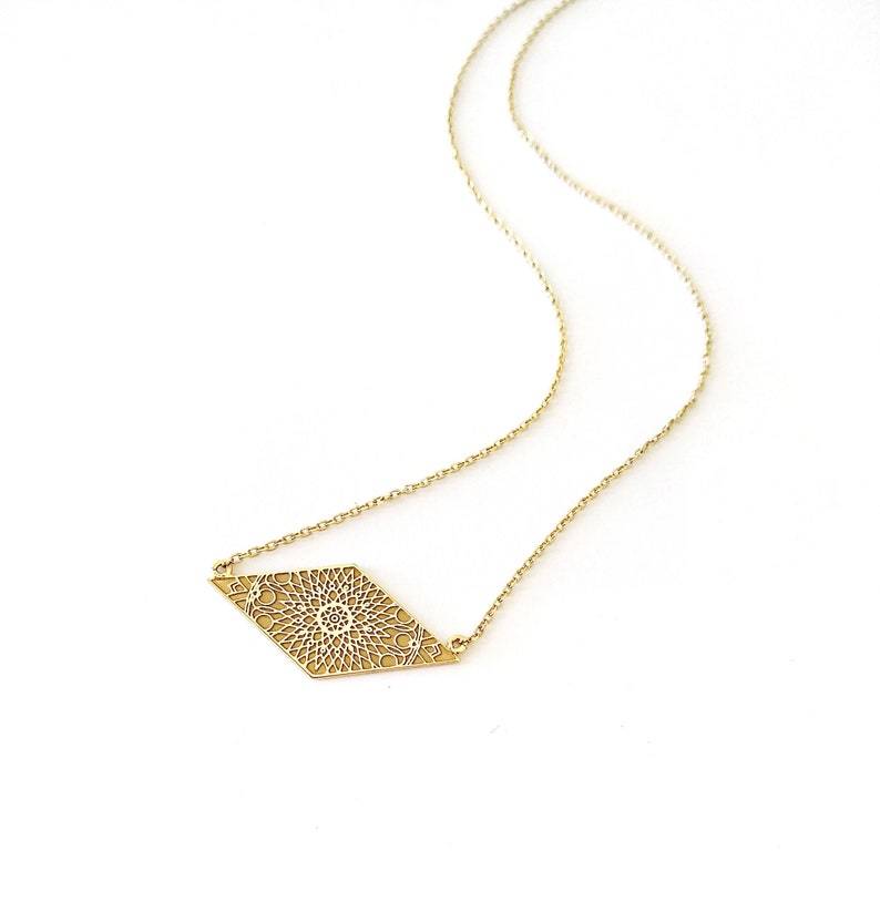 May include: A gold necklace with a delicate, intricate diamond-shaped pendant featuring a circular design.