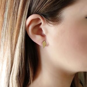 May include: A pair of gold diamond-shaped stud earrings. The earrings are small and simple, making them a versatile accessory for any occasion.