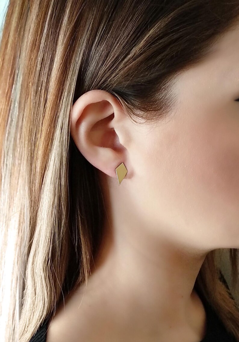 May include: A pair of gold diamond-shaped stud earrings. The earrings are small and simple, making them a versatile accessory for any occasion.