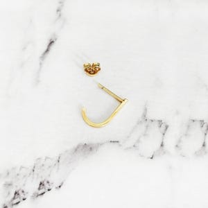 May include: A pair of gold hoop earrings. One earring is a simple hoop, the other is a small, curved hoop.