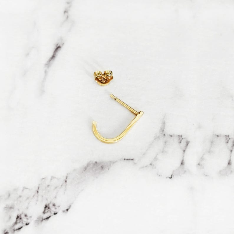 May include: A pair of gold hoop earrings. One earring is a simple hoop, the other is a small, curved hoop.