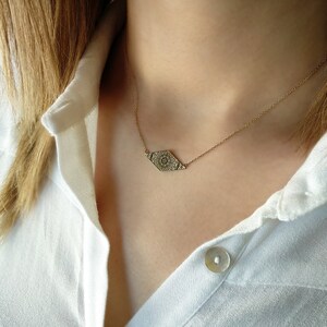 May include: A gold chain necklace with a delicate, patterned pendant in the shape of a diamond. The pendant has a detailed, intricate design.