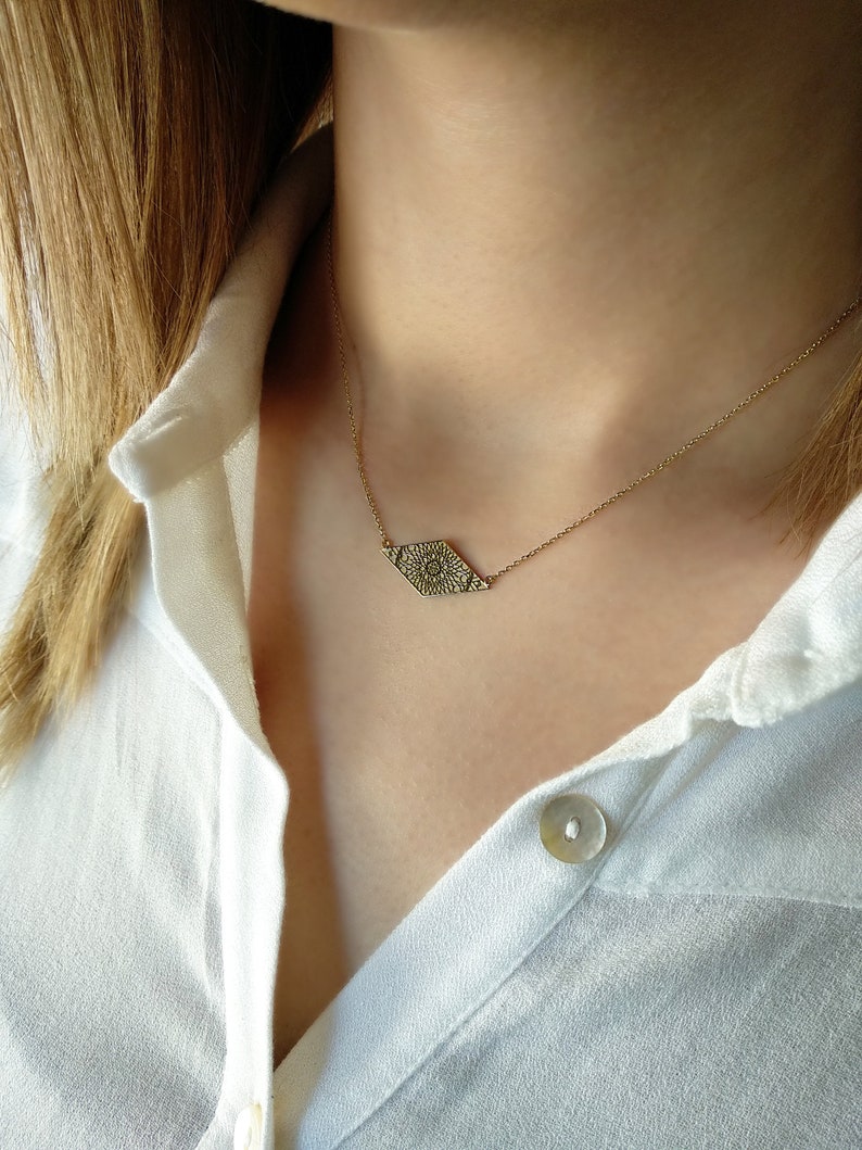May include: A gold chain necklace with a delicate, patterned pendant in the shape of a diamond. The pendant has a detailed, intricate design.