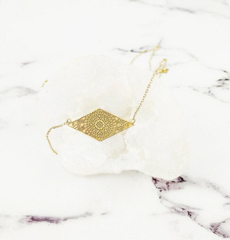 May include: A gold necklace with a diamond-shaped pendant featuring a detailed mandala design.