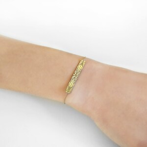 Op de afbeelding: Een gouden armband met een delicate ketting en een geometrisch ontwerp.