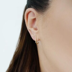 May include: A close-up of a person's ear with two gold earrings. The larger earring is a simple hoop, while the smaller earring is a curved shape.