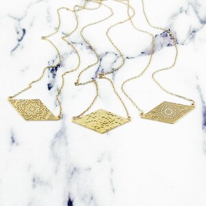 May include: Three gold necklaces with diamond-shaped pendants. The pendants feature different designs, including a mandala, a hammered texture, and another mandala.