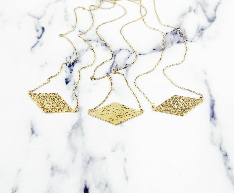 May include: Three gold necklaces with diamond-shaped pendants. The pendants feature different designs, including a mandala, a hammered texture, and another mandala.
