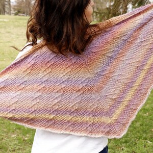 Könnte beinhalten: Ein farbenfroher gestrickter Schal mit einem Farbverlauf von Lila, Orange und Gelb. Der Schal ist über die Schultern einer Person gelegt und mit einem strukturierten Stich gearbeitet.