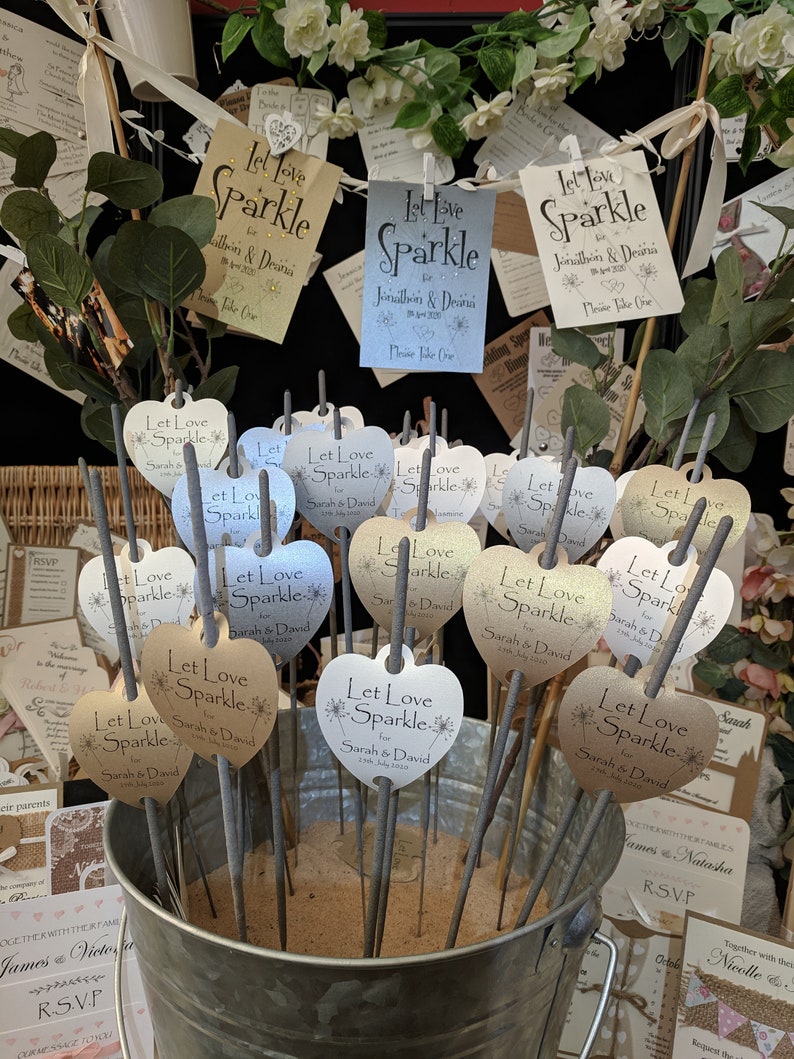 May include: A silver bucket filled with sand and heart-shaped sparklers. The sparklers have labels that say "Let Love Sparkle" with the names "Sarah & David" and the date "2nd July 2020".