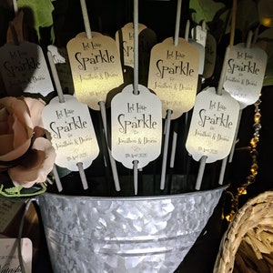 May include: A silver bucket filled with sparklers for a wedding. Each sparkler has a gold tag with the text "Let Love Sparkle for Jonathan & Deana 11th April 2020".