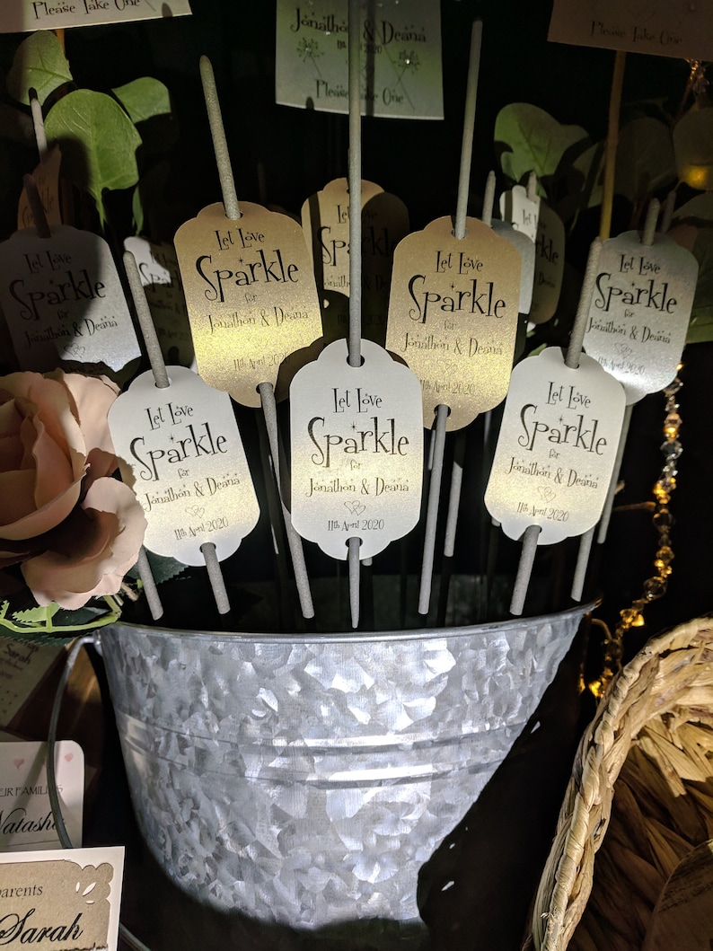 May include: A silver bucket filled with sparklers for a wedding. Each sparkler has a gold tag with the text "Let Love Sparkle for Jonathan & Deana 11th April 2020".