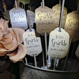 May include: A set of white and gold sparklers with tags that say "Let Love Sparkle for Jonathon & Deana 11th April 2020".
