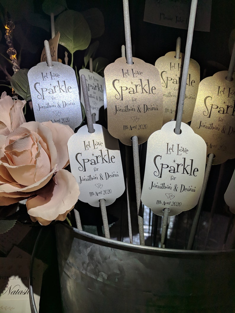 May include: A set of white and gold sparklers with tags that say "Let Love Sparkle for Jonathon & Deana 11th April 2020".