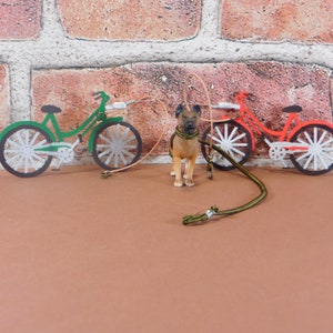 May include: A brown dog figurine with a green leash and two toy bicycles, one green and one red, on a brown surface.