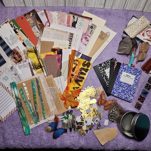May include: A collection of craft supplies including patterned paper, fabric scraps, ribbon, and a small metal container. The supplies are arranged on a purple surface.