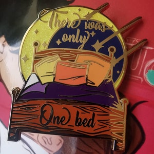 Puede incluir: Pin de esmalte dorado con un lecho con almohadas y un cielo estrellado. El texto "There was only one bed" est&aacute; escrito en la cama.